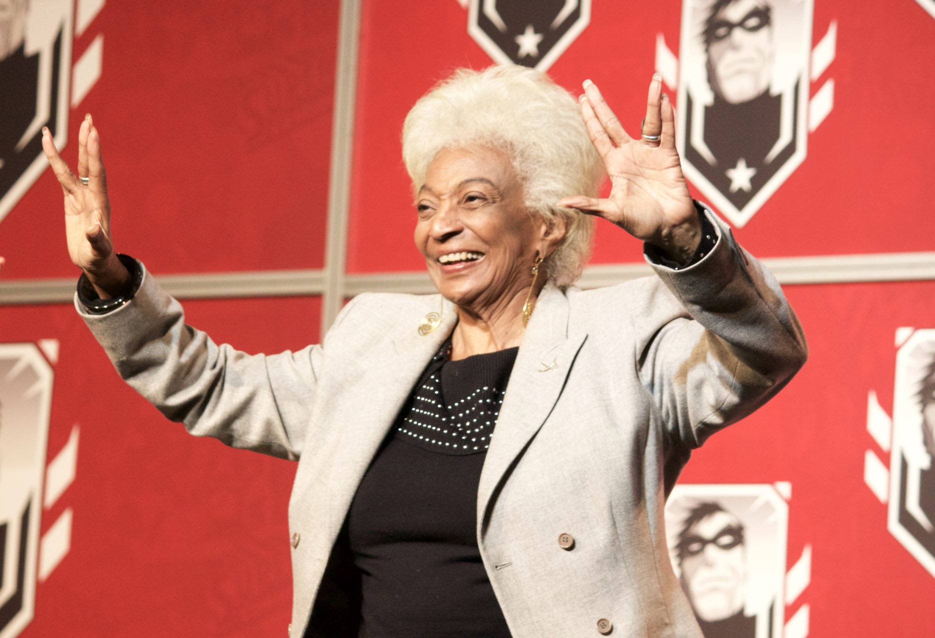 Nichelle Nichols giving the Vulcan salute with both hands on stage at a 2016 con