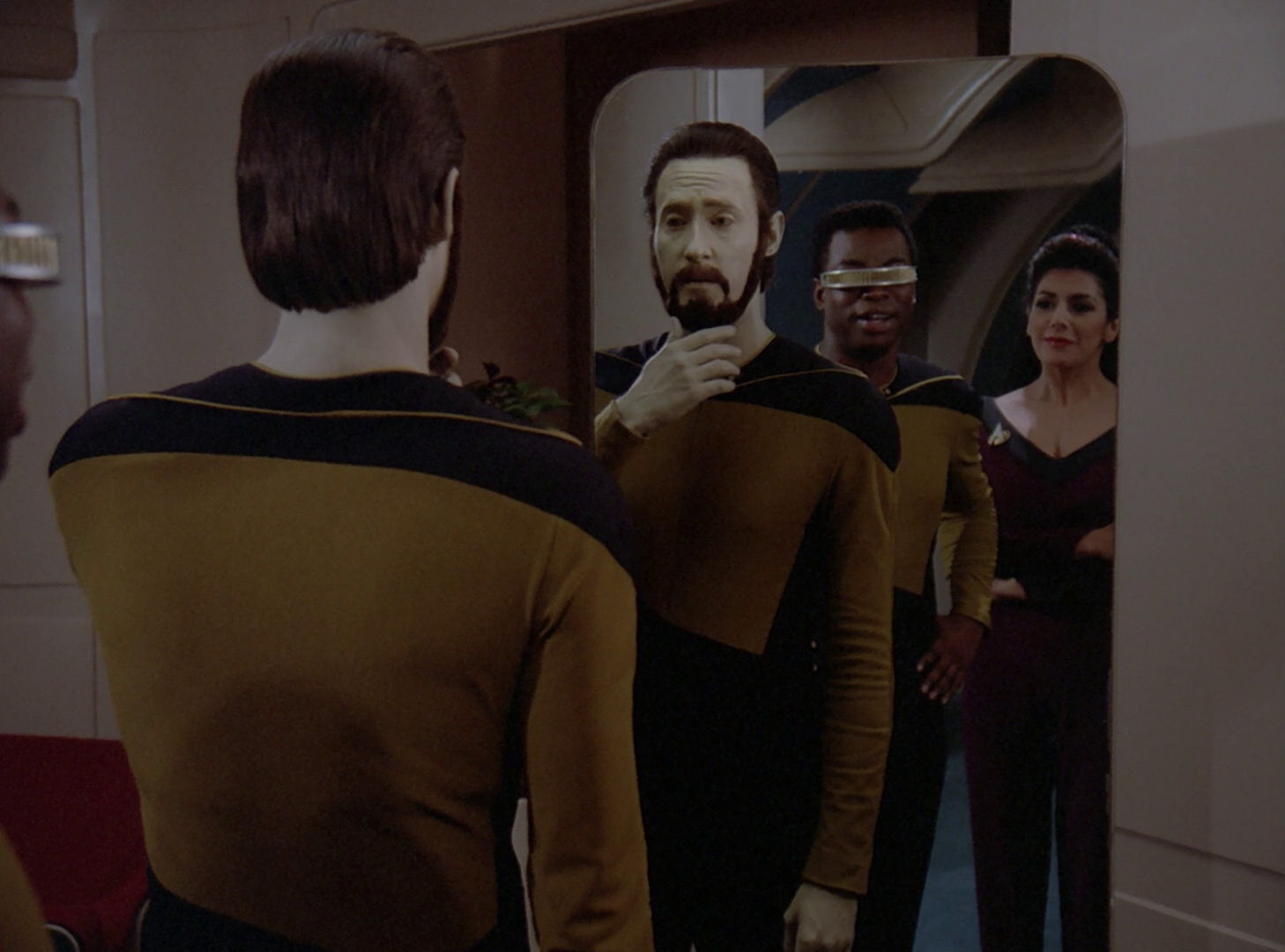 Data looking at his new beard in the mirror, while Geordi and Troi watch