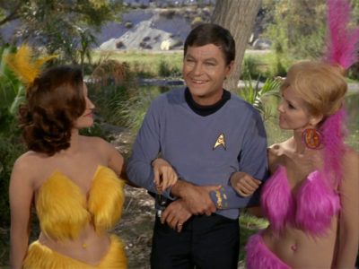 Bones in Shore Leave with two women on his arm, both wearing brightly coloured fur bikinis